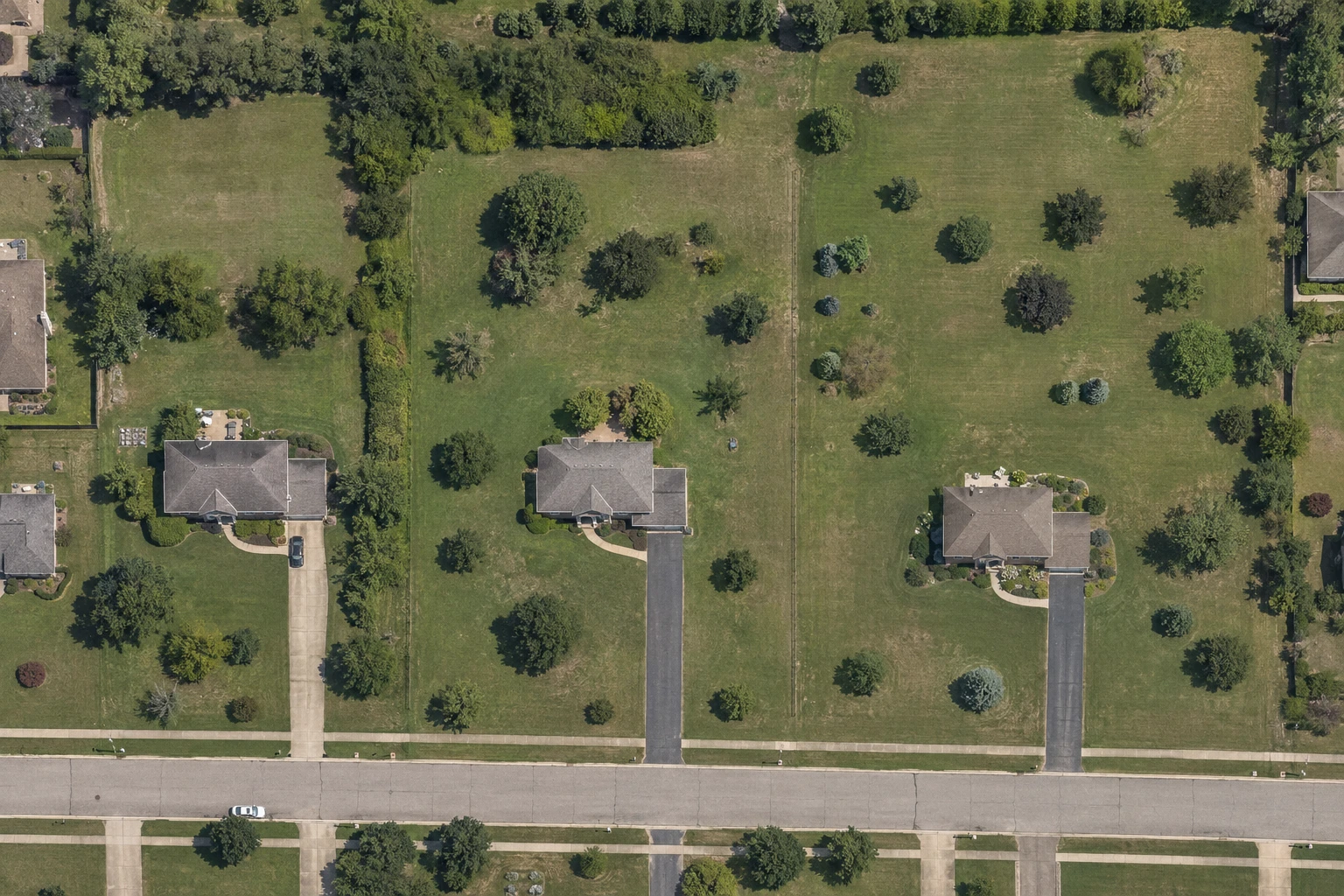 Three neighbouring residential properties photographed from above with their lot boundaries traced, each one larger than the last: a quarter-acre lot, a half-acre lot, and a one-acre lot.