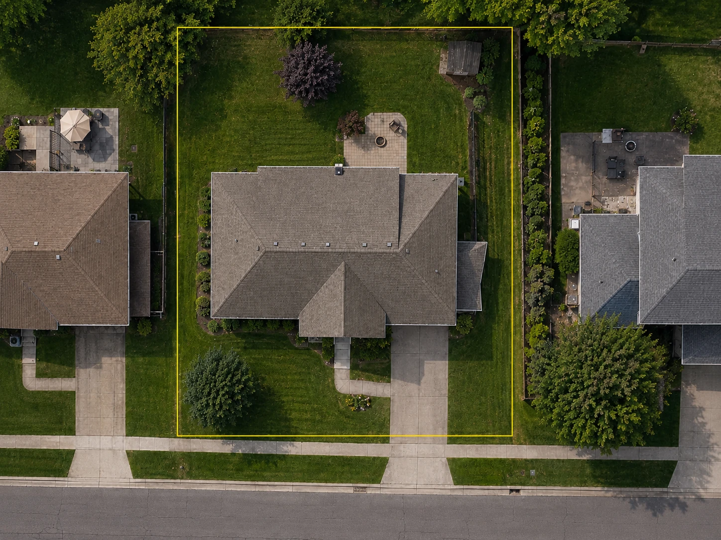 Aerial view of a residential property with its mapped parcel boundary drawn in yellow, running close to but not exactly along the fences, mowing edge and hedge visible on the ground beside it.