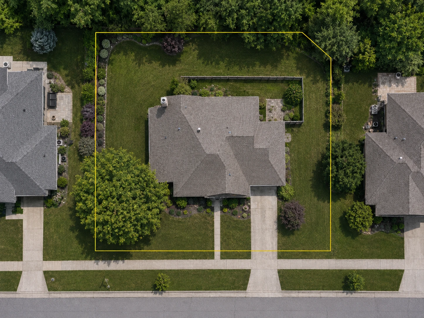 Aerial view of a residential property with its parcel boundary drawn in yellow, a fence standing well inside that boundary, and a public sidewalk running outside it.